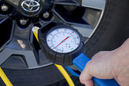 Person checking tire pressure with a Analogue Tyre Inflator gauge on a car tire, demonstration image.